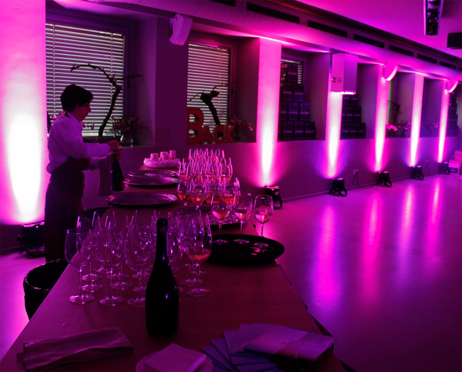 Mesa para servicio con copas y vino con el ambiente decorado en violeta en la sala BACK